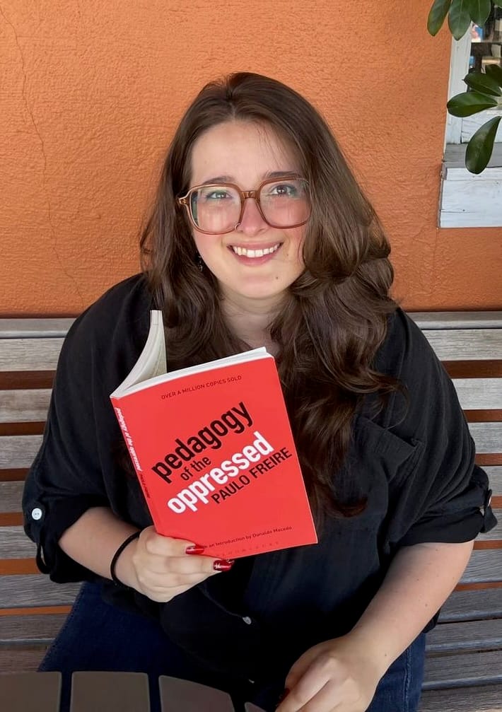Headshot of Anna Platt holding a copy of the book "Pedagogy of the Oppressed"
