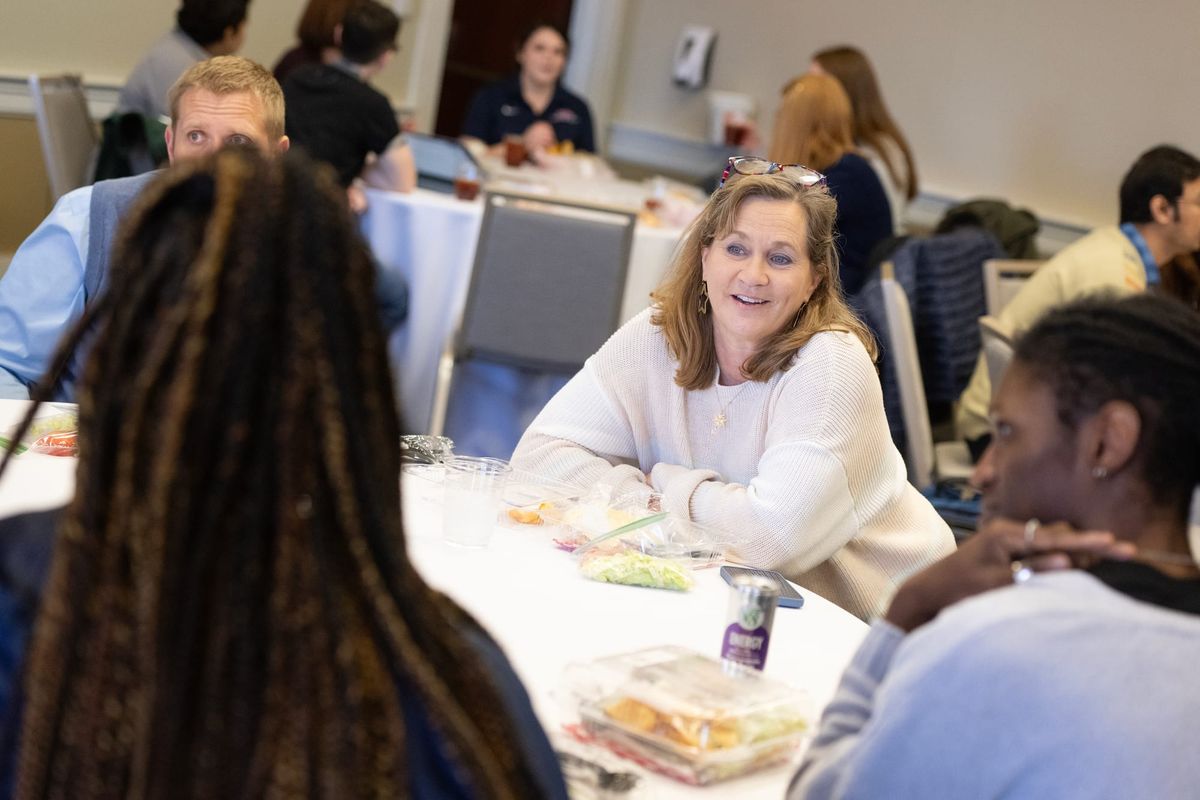 Instructors discuss teaching while sitting at round tables in a meeting room.