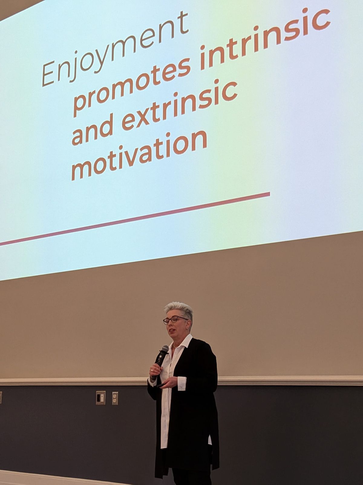 Flower Darby speaks. Behind her and projected on the wall is a slide that reads, "Enjoyment promotes intrinsic and extrinsic motivation."