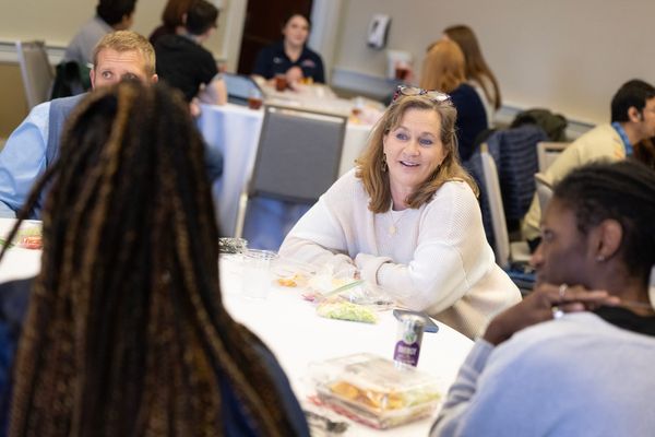 Instructors discuss teaching while sitting at round tables in a meeting room.