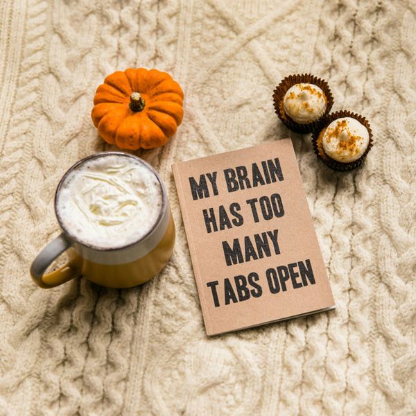 a mug of coffee, a pumpkin, and a fuzzy fall sweater adorn a sign that says, "My brain has too many tabs open."