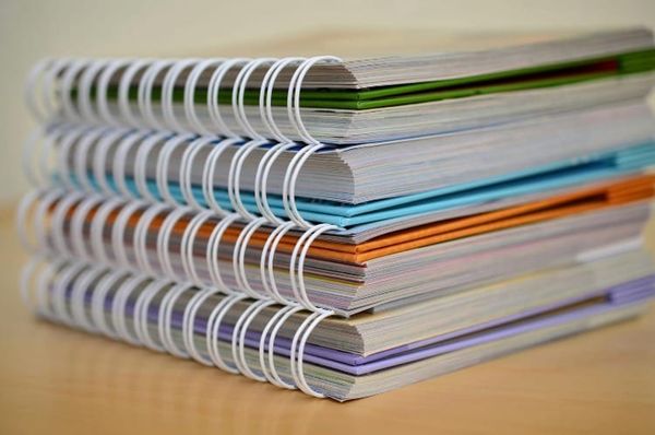 A stack of notebooks sits atop a table. They have different colored binding and white spirals.