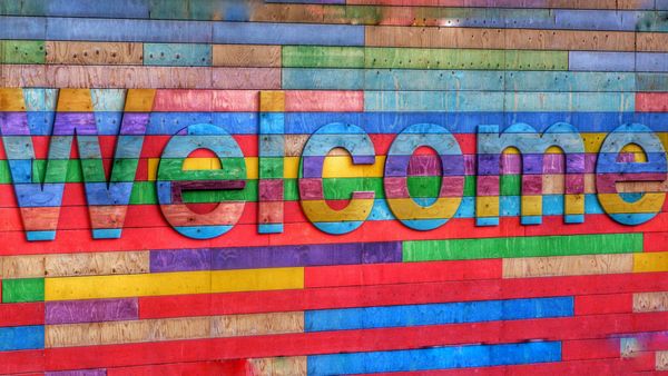 The word "welcome" appears on a wall constructed of multicolored wood planks.