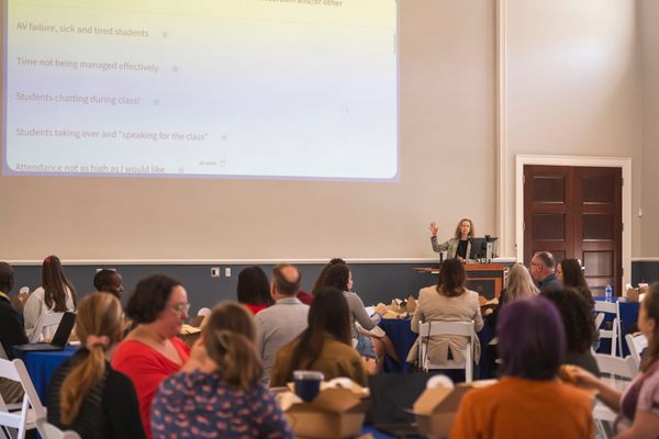 A group of people sitting at round tables eating lunch listen to speaker Jessamyn Neuhaus.