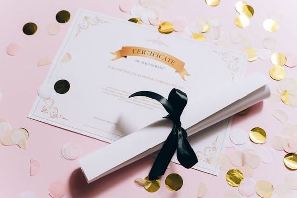 A certificate appears beneath a rolled piece of paper secured by a black ribbon.