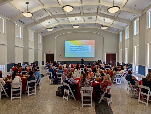 A room full of instructors seated at round tables with slides projected at the front.