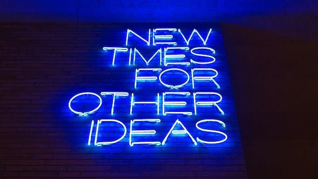 Blue neon sign reading "NEW TIMES FOR OTHER IDEAS" on a brick wall