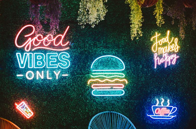Vibrant neon wall art with positive messages including 'Good Vibes Only' and food-themed signs creating a cheerful, welcoming atmosphere