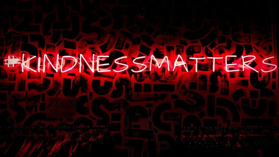 Red neon sign reading “Kindness Matters” against a dark background with layered graphic textures.