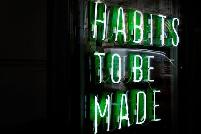 Green neon storefront sign reading 'Habits to be Made' against a dark background with reflections in the glass