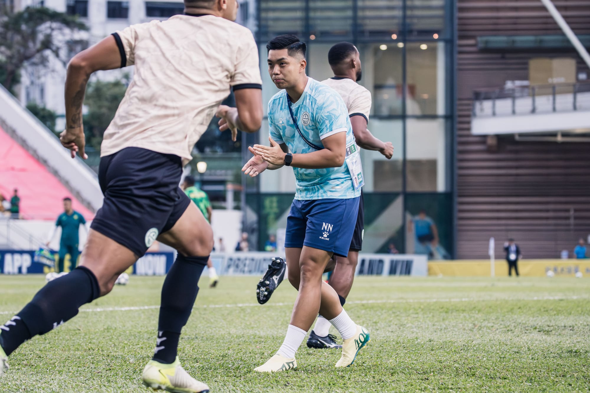 Norris Ng in a light blue Tai Po FC training shirt with NN-monogrammed shorts running through a warm-up drill alongside a Tai Po player at the AFC Champions League Two.