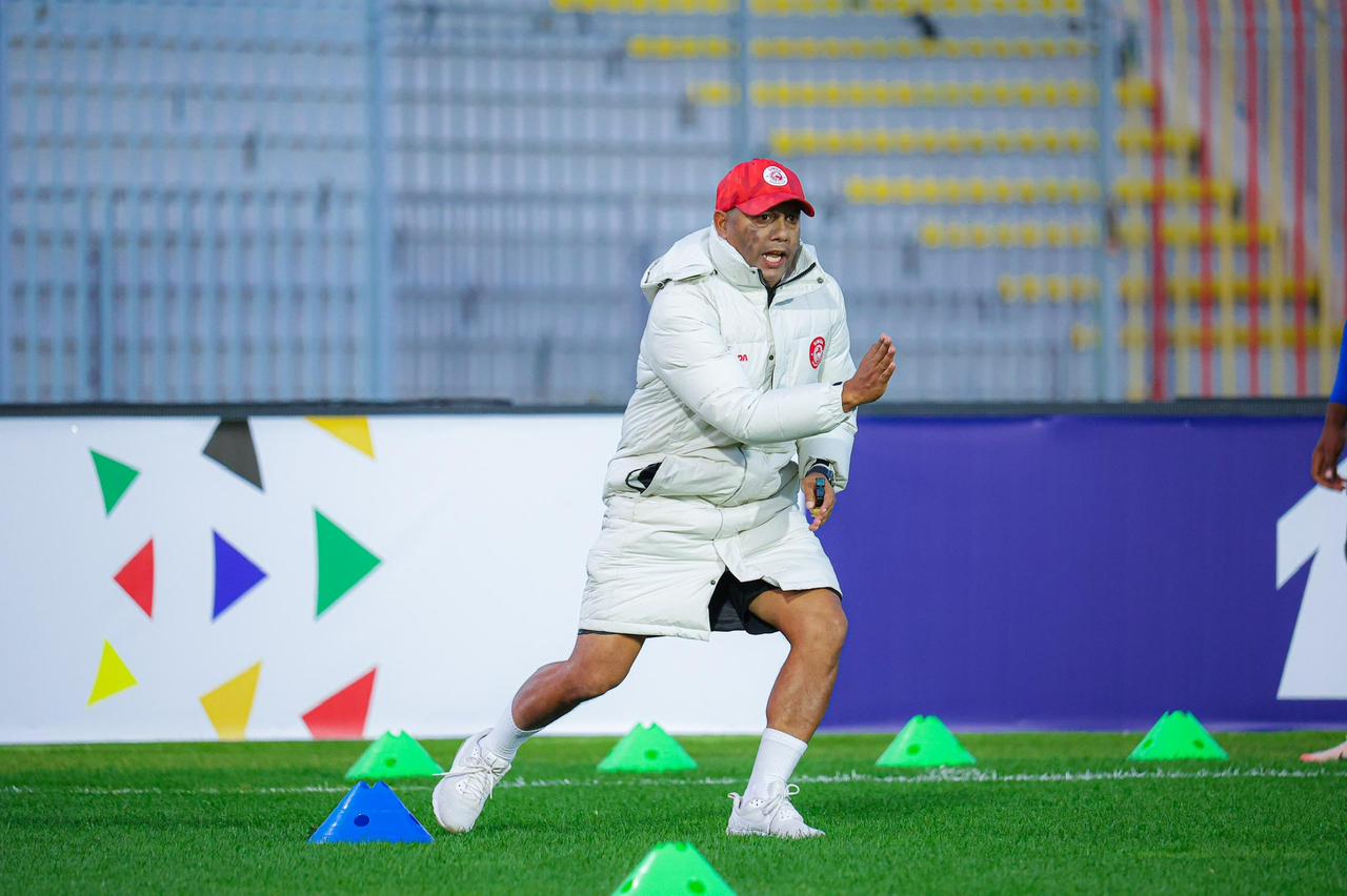 Riedoh Berdien in a long white puffer jacket and red Simba cap mid-stride through coloured agility cones during a cold-weather training session.