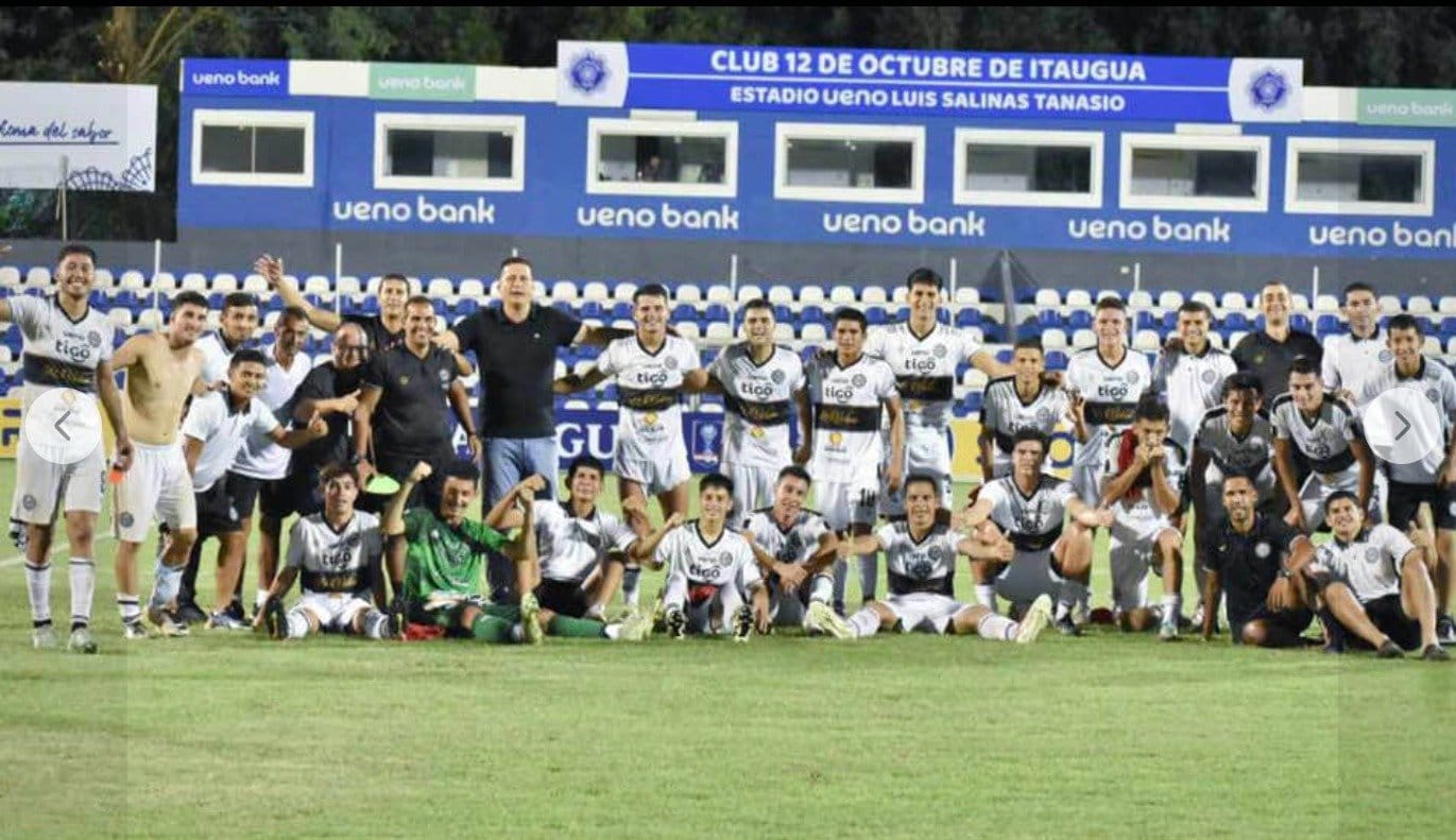 A celebration team photo of a Paraguayan youth squad at Estadio Ueno Luis Salinas Tanasio, with Marco Gracia in a black polo at the back of the group.