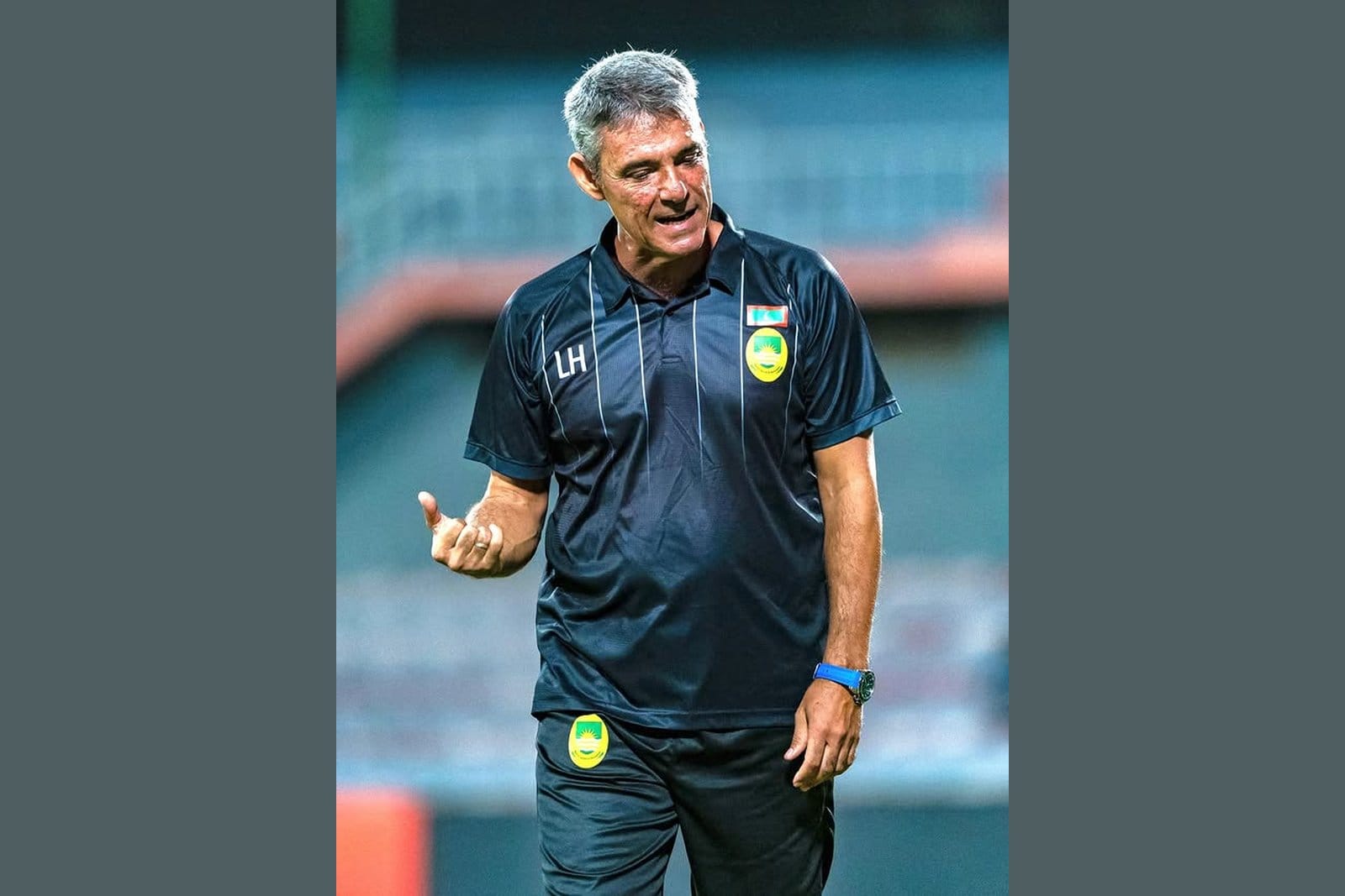 Luisma Hernández in a dark navy Maziya S&RC training polo with "LH" initials, gesturing during a training session under stadium lights.