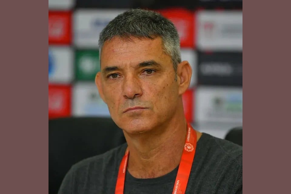Luisma Hernández seated in front of a sponsor backdrop with an orange "Uzbekistan" lanyard, addressing a press conference during his tenure as head coach of Metallurg Bekobod.
