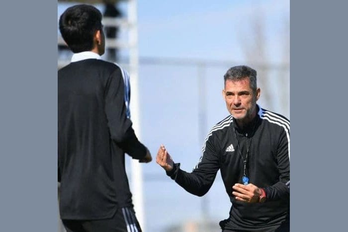 Luisma Hernández in adidas training kit on an outdoor pitch, gesturing as he speaks with a player in profile, during his coaching tenure in South Korea.
