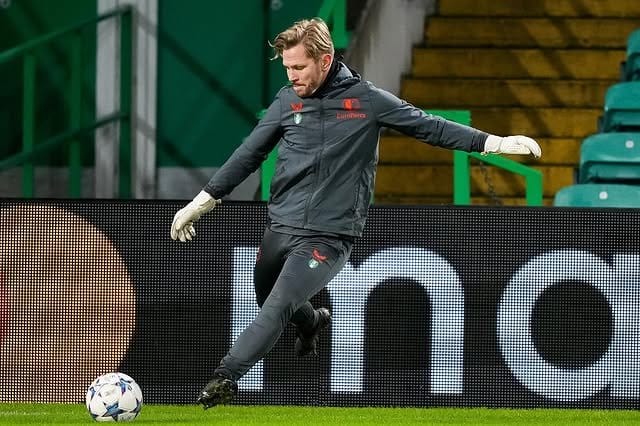 Jyri Nieminen in Feyenoord training kit and goalkeeper gloves, striking a ball with his right foot in front of a stadium's advertising boards and green stands.