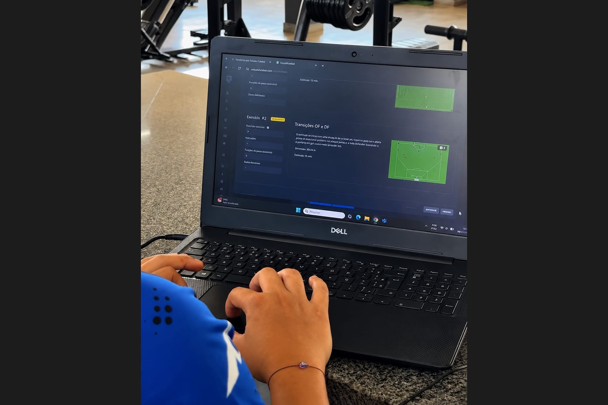 A laptop on a desk showing a football training-platform screen with drill descriptions and pitch diagrams, a person typing.