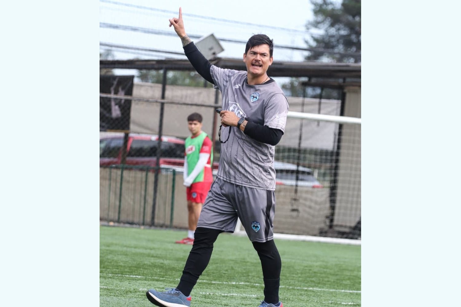 Manuel Sánchez in a grey and light-blue CSD Cajón del Maipo coaching kit, pointing up with his right hand while directing his team during a training session on an artificial pitch.