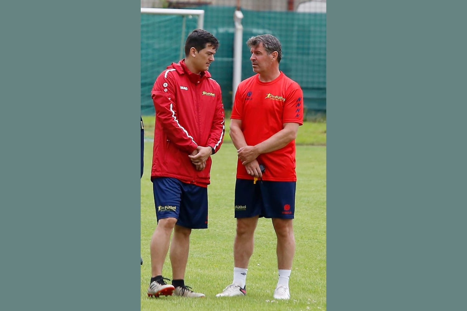 Manuel Sánchez, on the left in a red Pro Fútbol Analytics jacket, in conversation with a senior colleague in a red Pro Fútbol Analytics shirt on a training pitch.