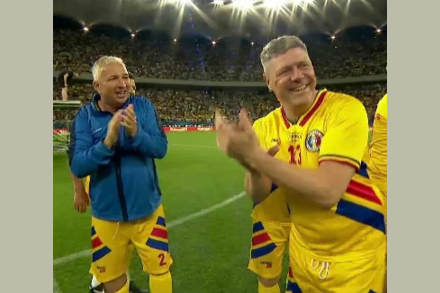 Tibor Selymes applauding on the pitch in Romania's yellow kit alongside another former international at a legends match.