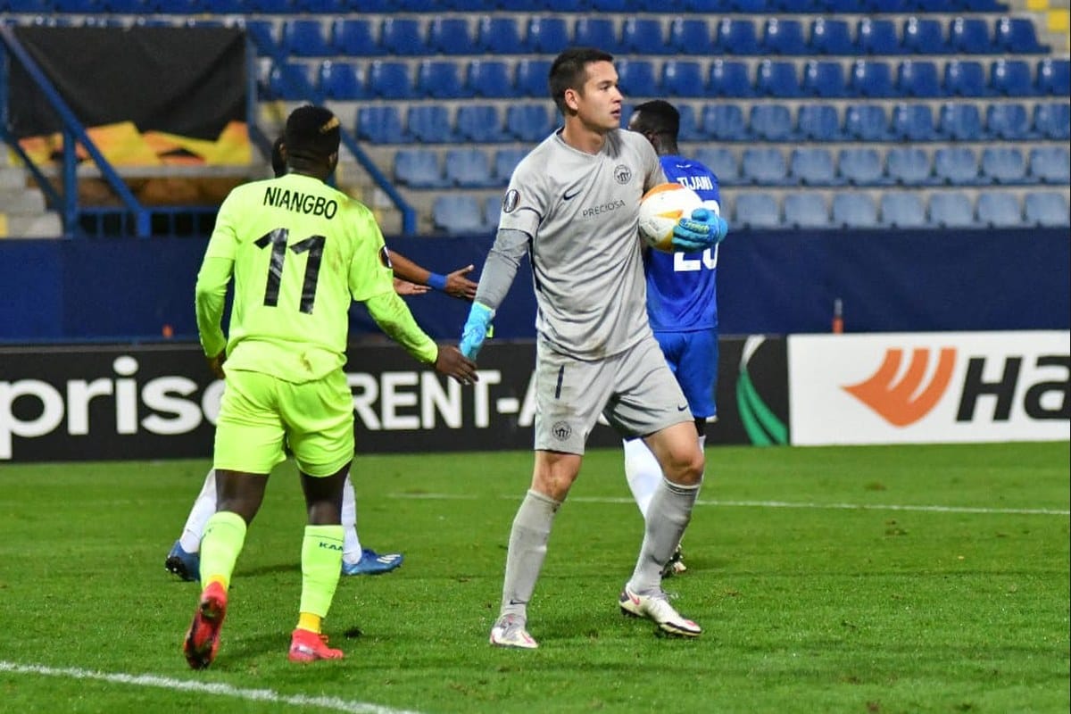 Filip Nguyen in Slovan Liberec's grey goalkeeper kit, holding the ball to his chest in front of an opponent in a yellow kit numbered 11, during a UEFA Europa League group-stage match in the 2020-21 season.