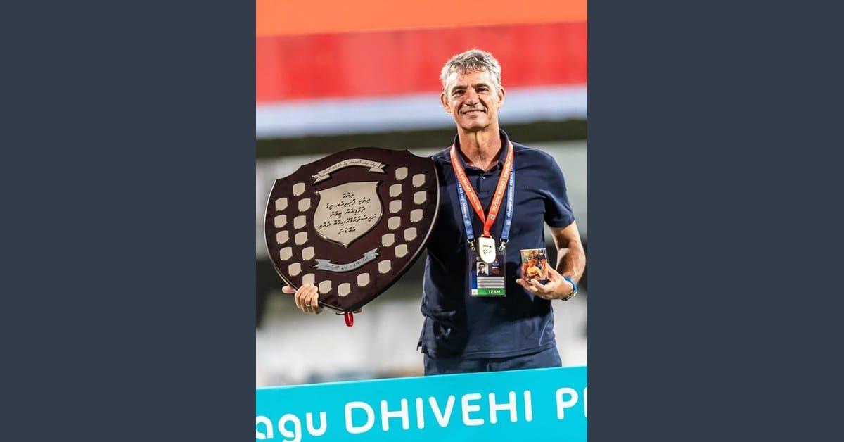 Luisma Hernández, Spanish UEFA Pro coach, in a navy Maziya polo with a winner's medal, holding the Dhivehi Premier League championship shield after winning the 2025/26 Maldives title.