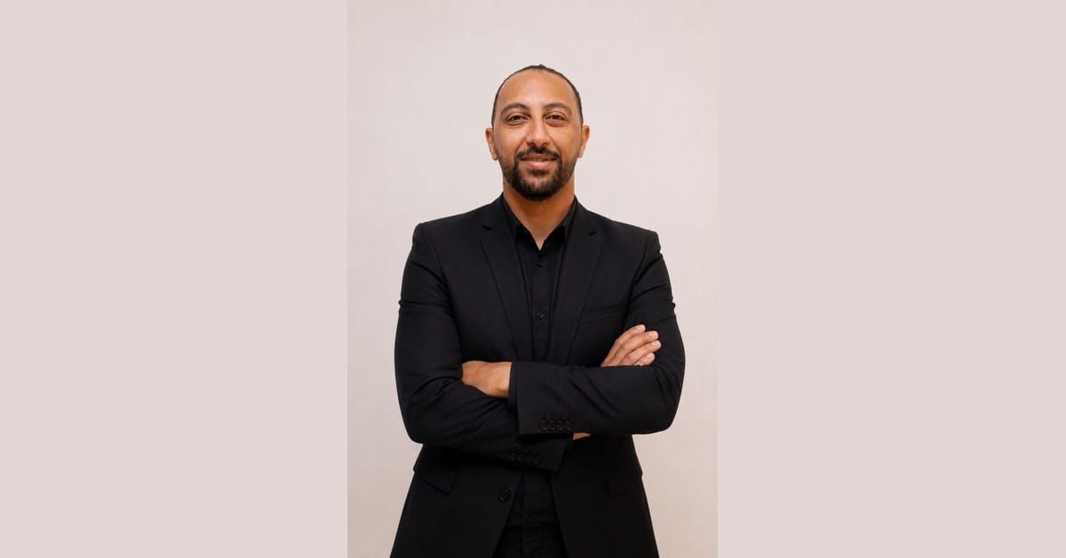 Sameh Abdelghany, Egyptian football performance analyst, in a black suit with arms folded, smiling at the camera against a beige studio background.