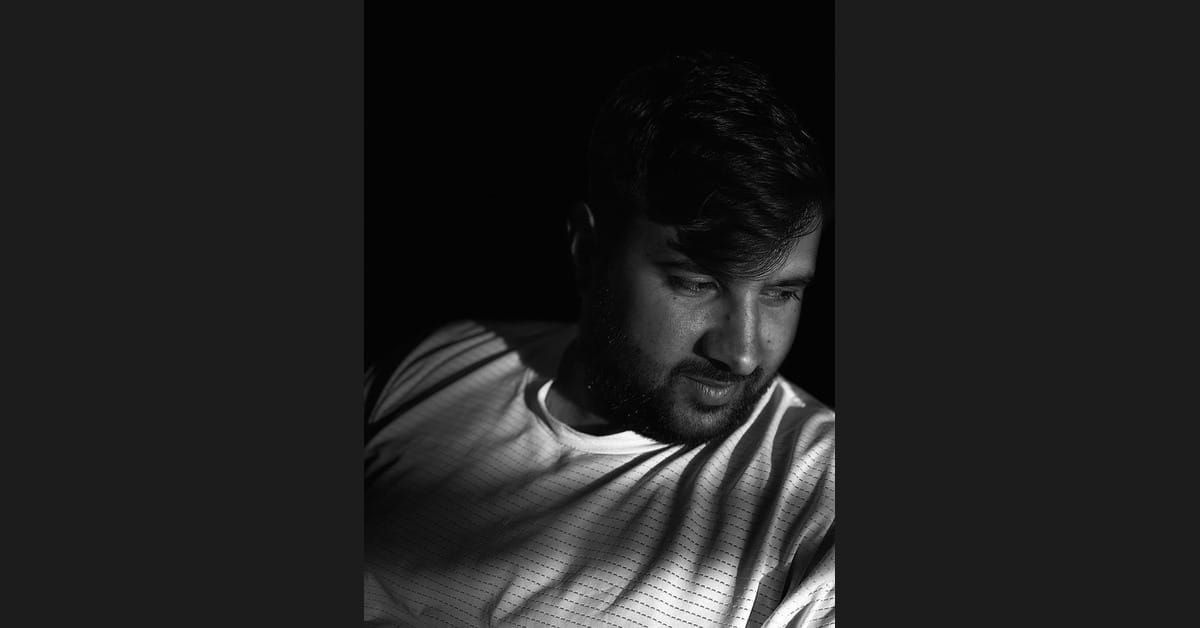 Tahir Salayev, Azerbaijani football coach and analyst, in a dramatic black-and-white portrait, looking down in a textured training top against a dark background.
