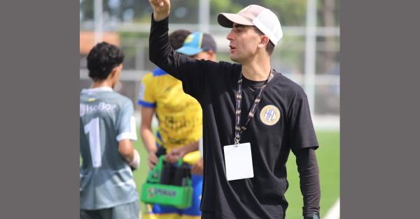 Marco Gracia, Chilean head coach, in a black Herrera FC shirt and CONCACAF lanyard, raising his arm to communicate with a player from the touchline.