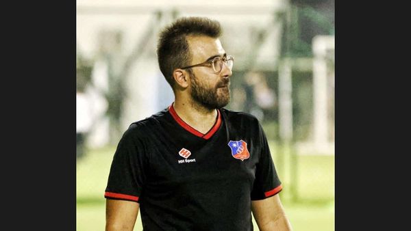 Rui Gomes, Portuguese football coach with glasses and a dark beard, in a black HH Sport polo with red trim, looking to one side during a youth football match.