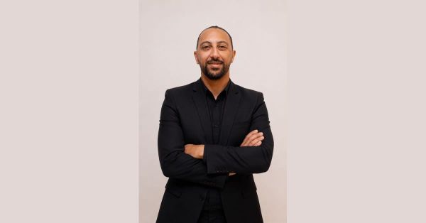 Sameh Abdelghany, Egyptian football performance analyst, in a black suit with arms folded, smiling at the camera against a beige studio background.