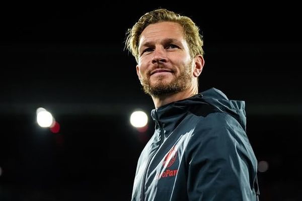 Jyri Nieminen, Finnish goalkeeper coach, in a dark Feyenoord jacket smiling under stadium floodlights during a match evening.