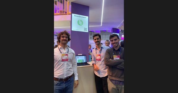 Three members of the ScoutDecision team standing beside their branded stand at Web Summit in Lisbon, smiling for the camera.
