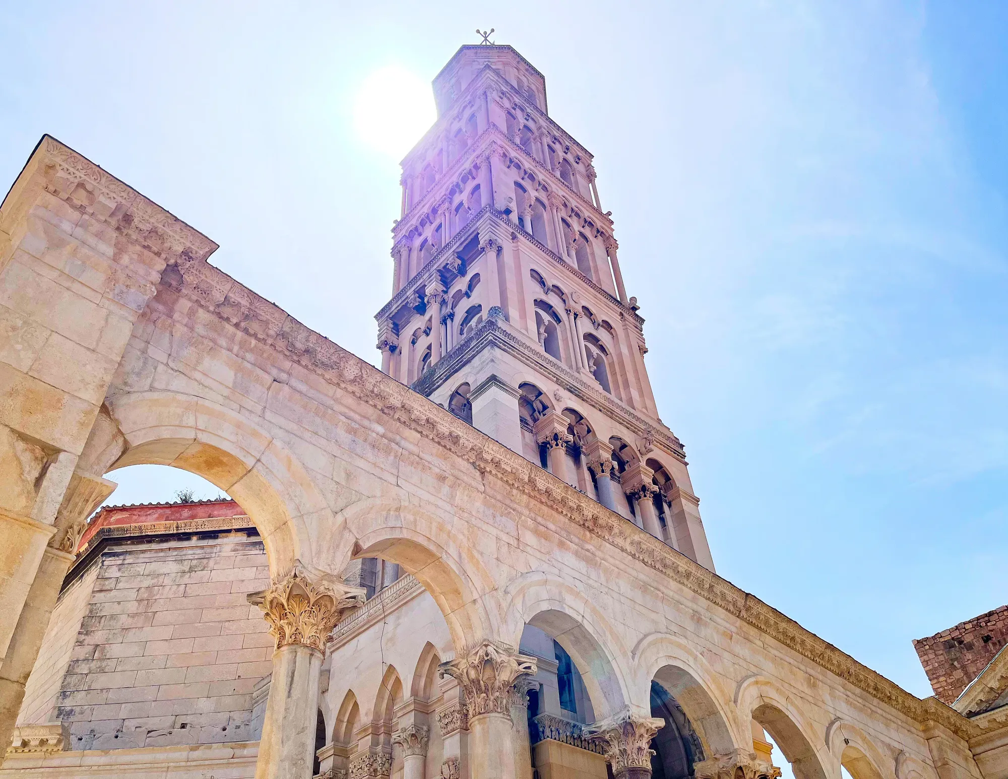 Tan stone tower set against the sun with arches in front of it