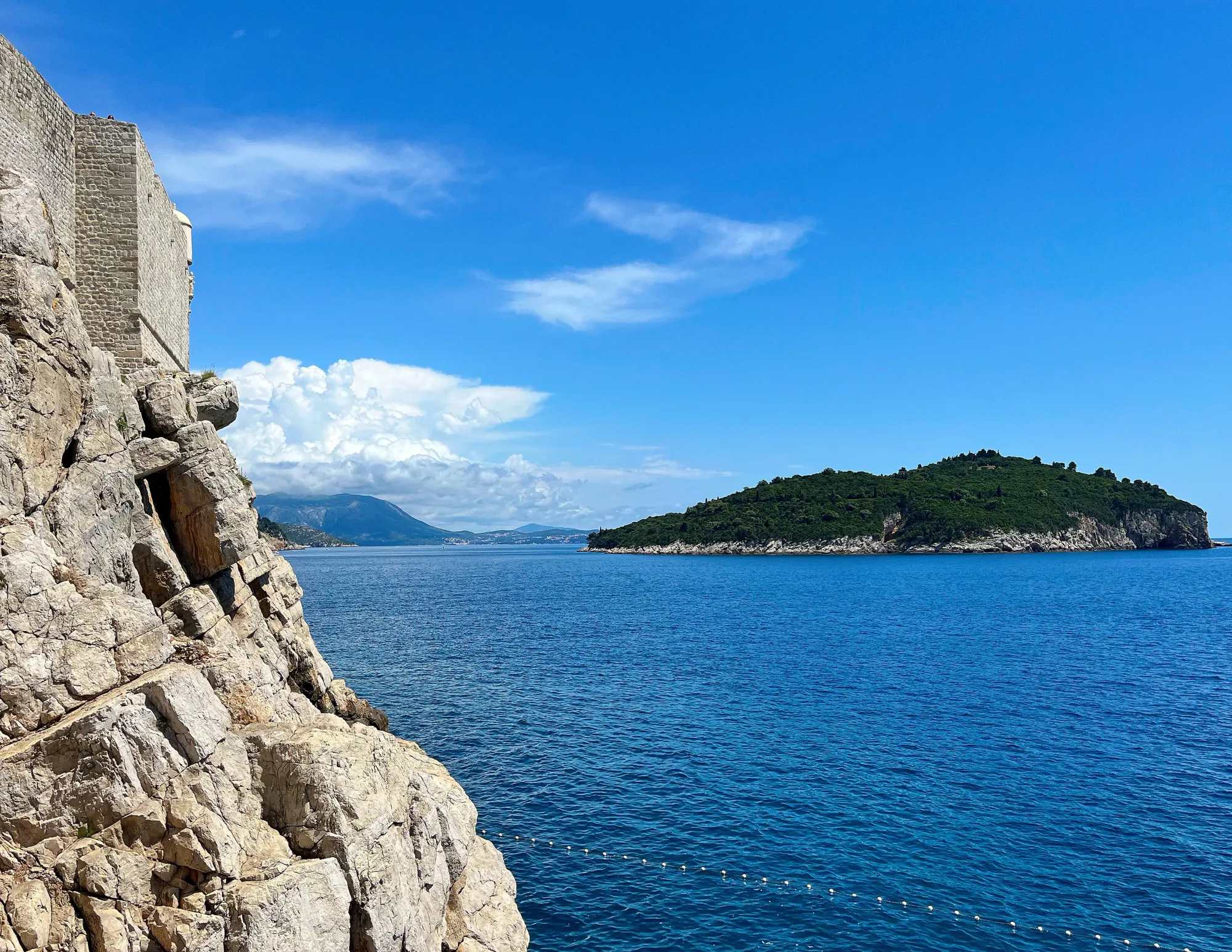 Stone walls set atop a stone cliff overlooking the blue sea with an island in the background