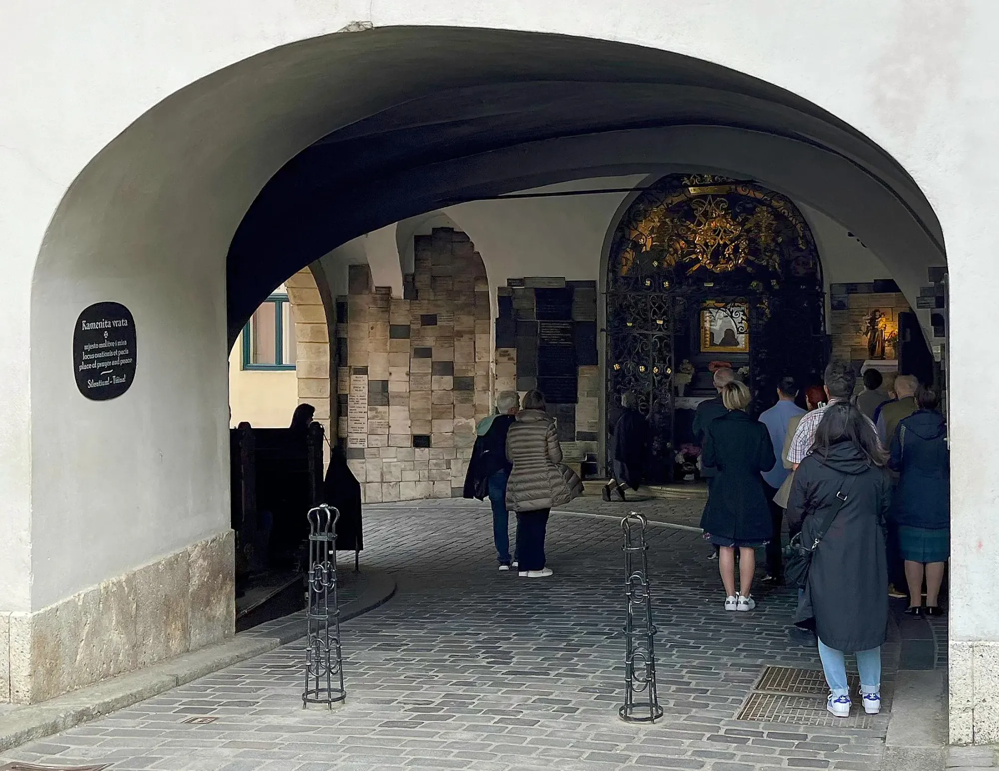 Arch-covered curved pathway with an ornate altar and a small crowd all standing in front of it