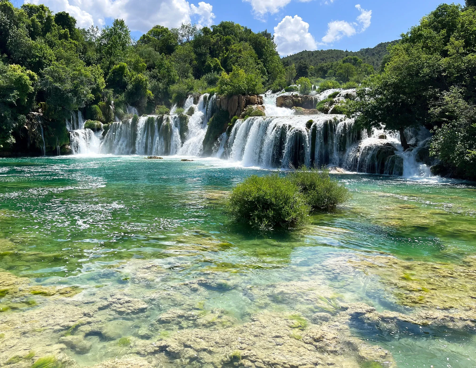 Cascading travertine surrounded by lush trees into green water