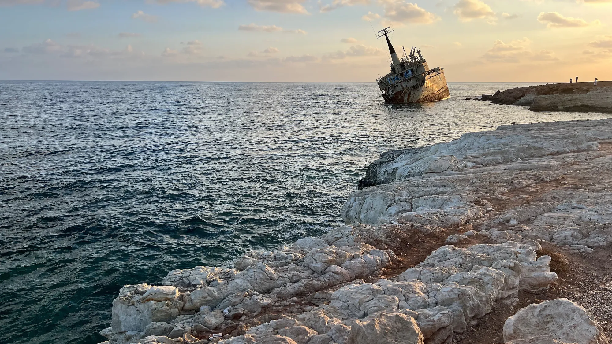 Rocky landscape seaside with a beached tilted cargo ship at sunset