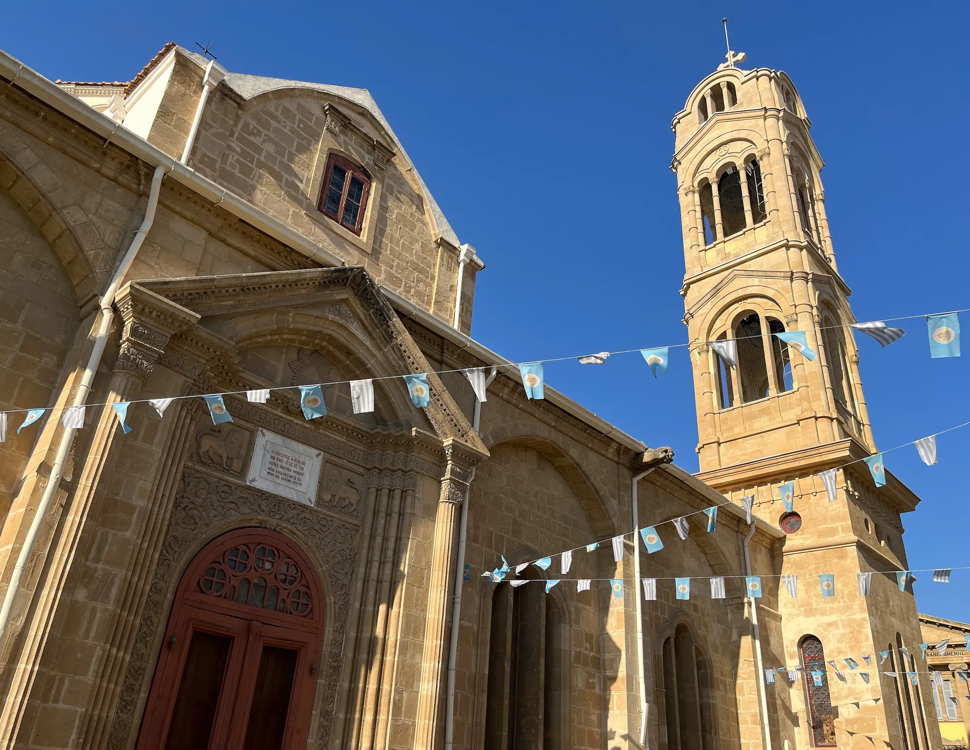 Tan stone church and tower with blue flags strung across the courtyard