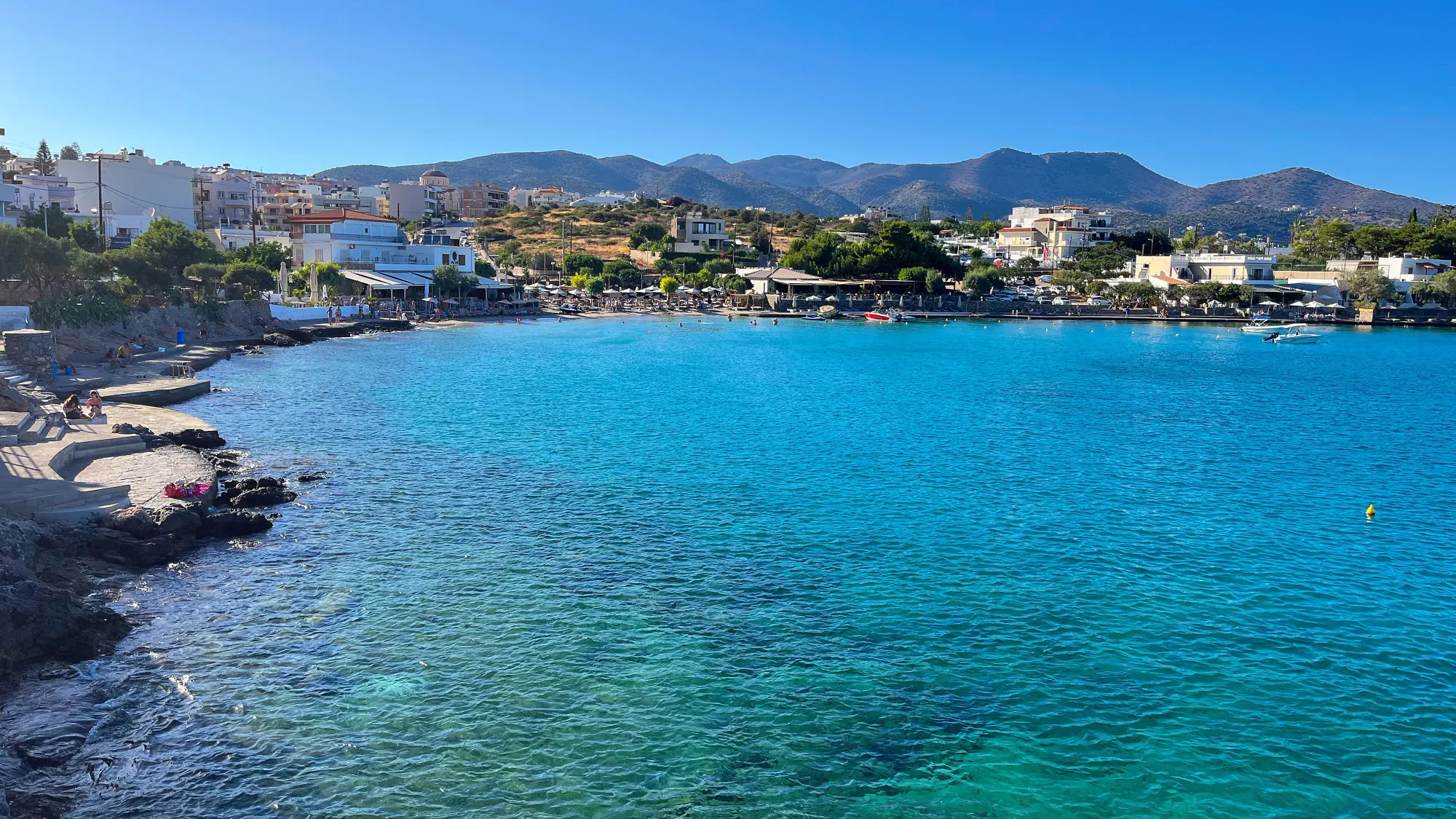 Multi-shades of blue water with stone and sandy spots filled with sunbathers and swimmers