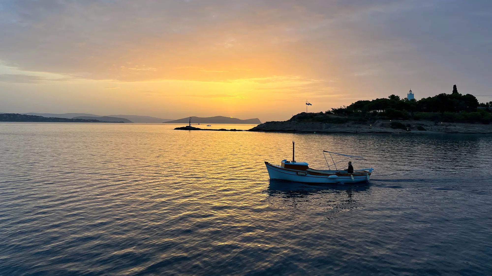 One lone boat cruising through a soft orange light as the sun sets against the edge of an island