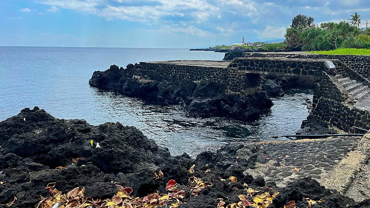 Black volcanic rocks with a stone bridge over them next to the water