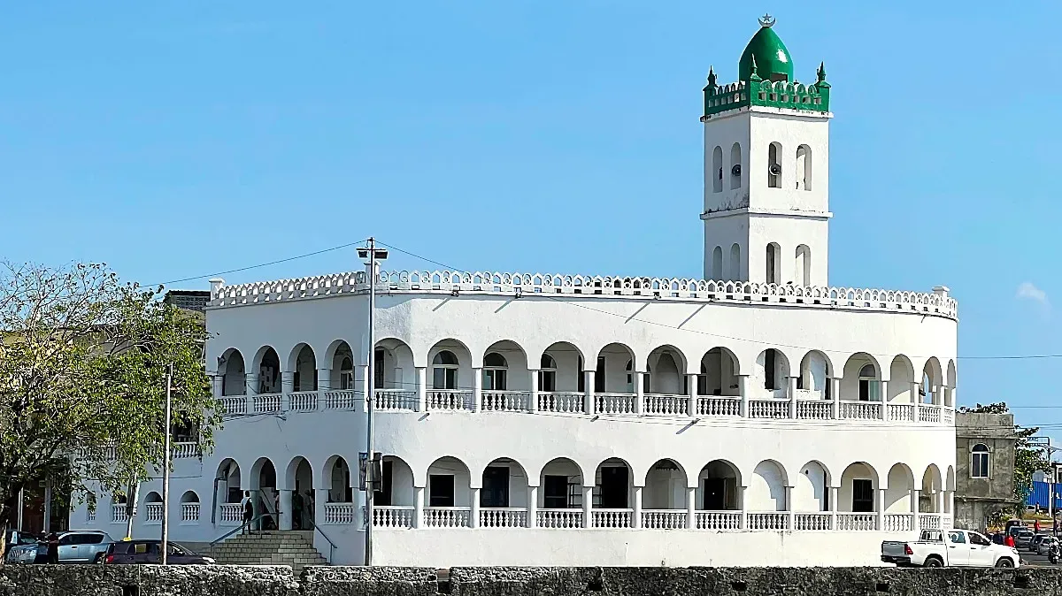 White arched building with a single tower covered in green