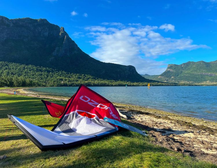 Pink and white kite resting on a grassy bank next to a lagoon and under the shade of a mountain