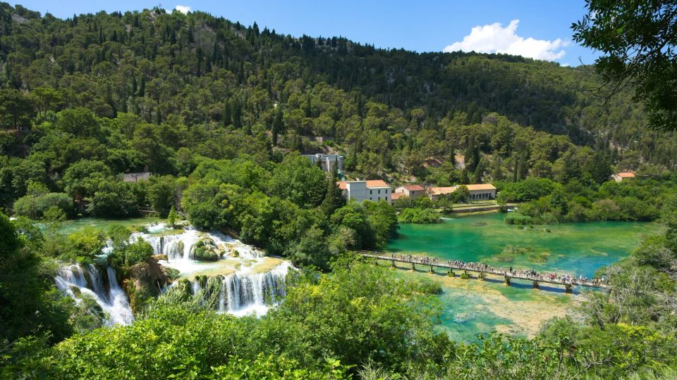 Waterfall in a lush green valley with a paneled walkway across the blue-green water