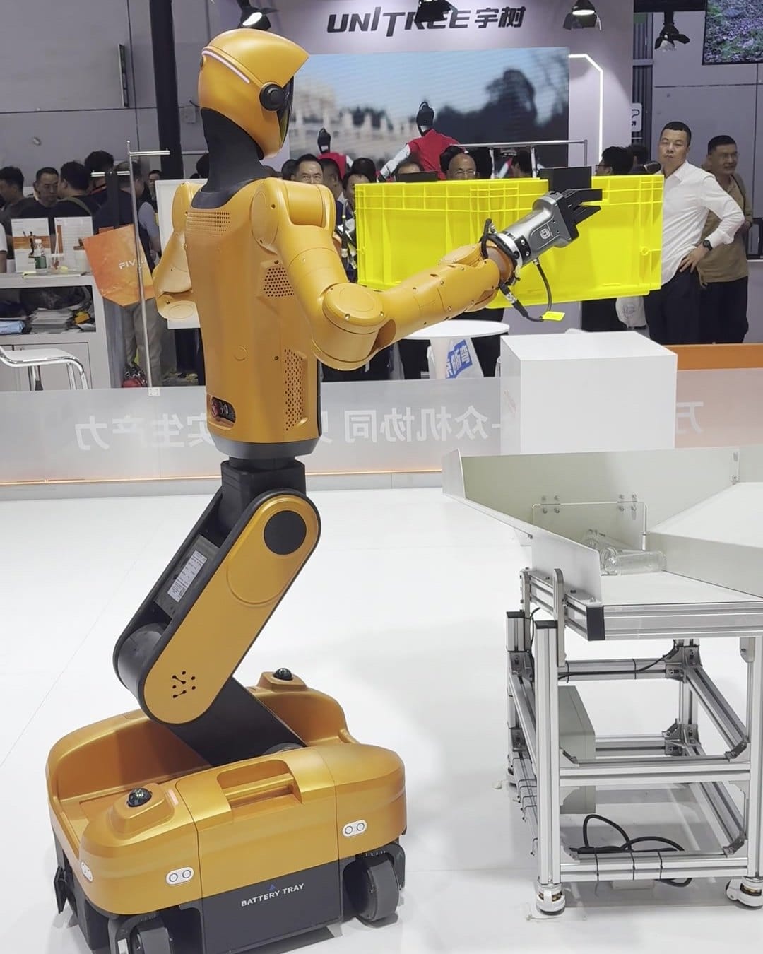 Orange wheeled humanoid moving a tote under the Unitree banner at CIIF 2026