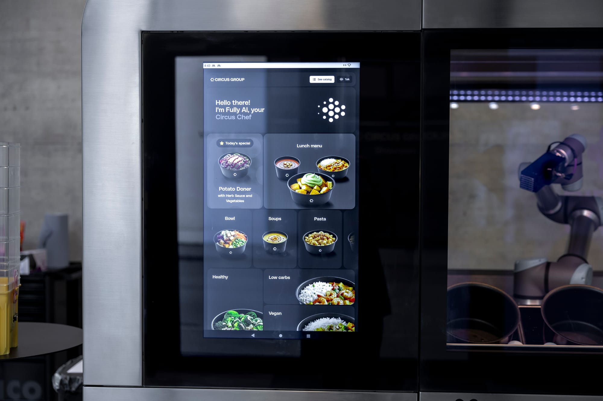 Close-up of the Circus Group CA-1 robot order screen beside a robotic arm inside the meal-production cell