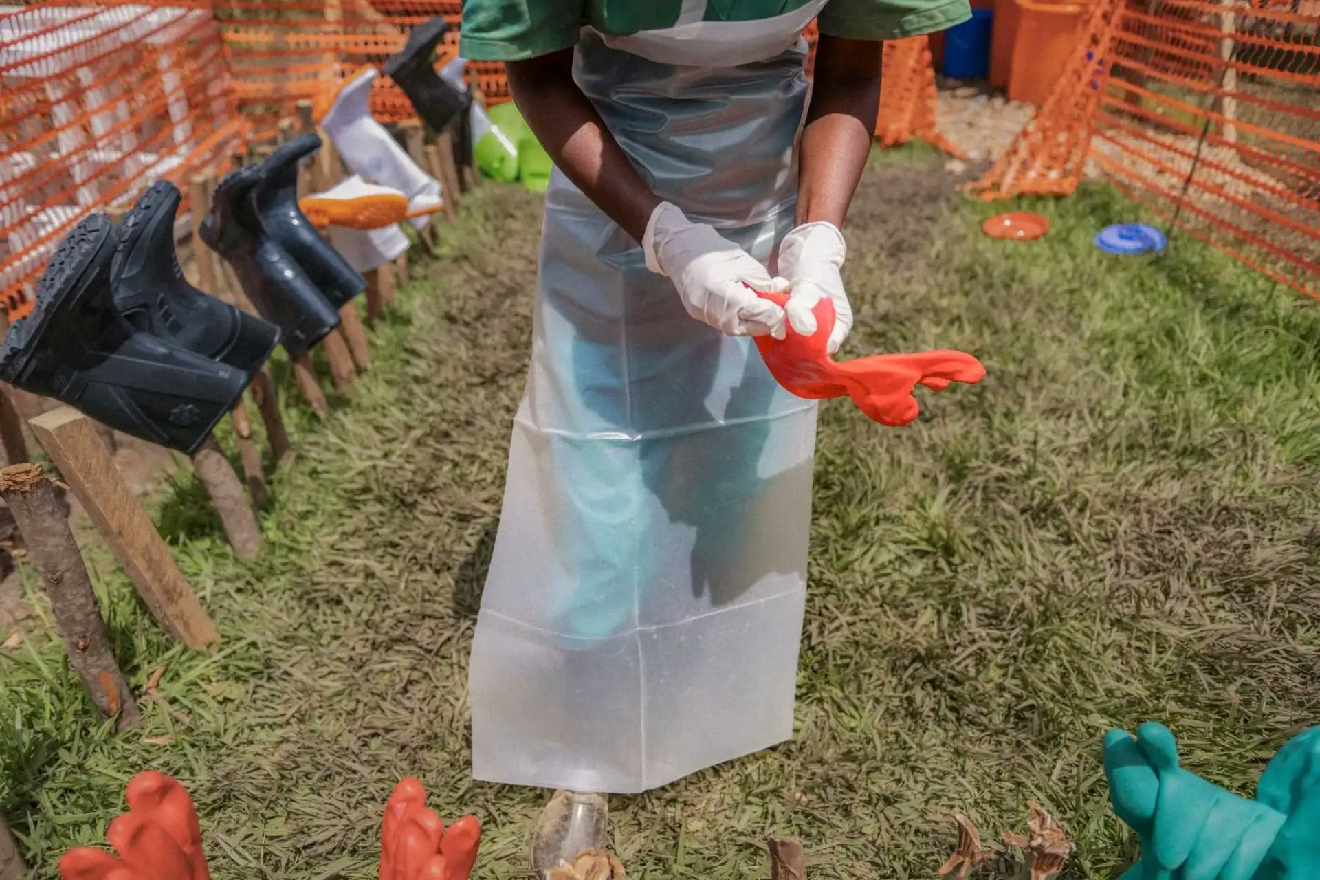Health worker in protective gear putting on a red glove inside an Ebola treatment-center enclosure.
