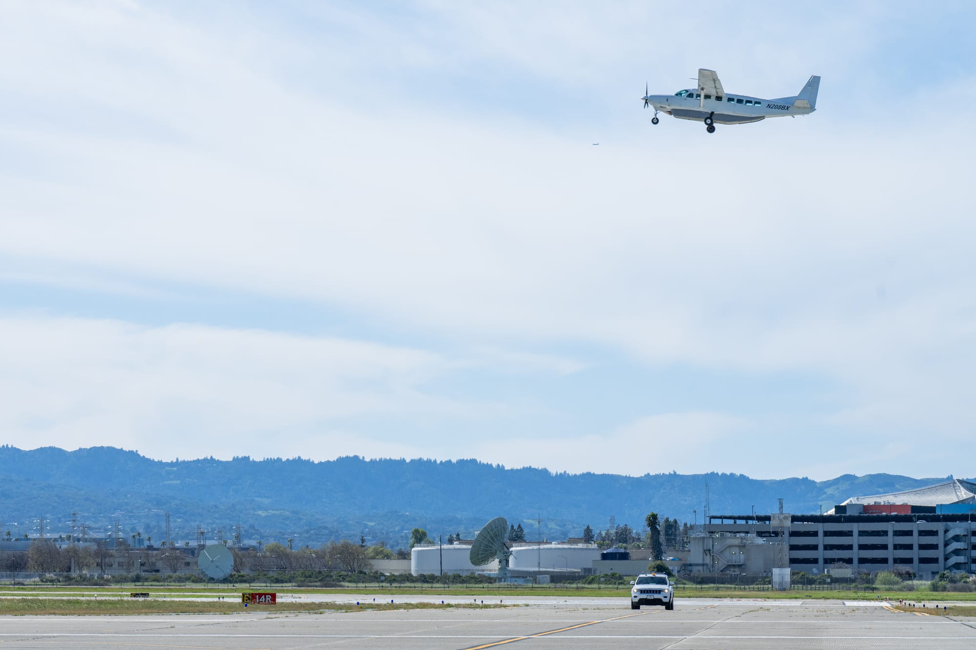 NASA aircraft flies above a runway while a vehicle sits on the runway below during autonomous runway safety testing.